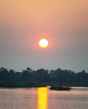 Küçük, dar motot teknesinde insan figürünün silueti Mekong 'un sakin ve huzurlu sularında sürükleniyor. Güney Laos' taki batan güneşten gelen suya yansıyan altın ışık huzmeleri arasında..