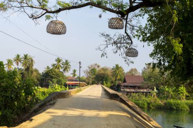 Don Khon Adası 'na doğru bakan, Fransız sömürge köprüsü boyunca, Mekong' u geçen, turistlerin geçmesi ya da dinlenmesi için popüler bir dönüm noktası ve gün batımı manzarası. Ağaçtan sarkan dekoratif ışıklar.