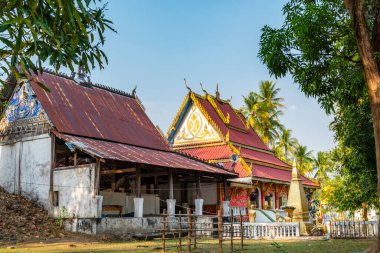 Don Khone adasındaki küçük Budist tapınağı. Güzel antik binalar, öğleden sonra, birçok yapraklı ağaçla çevrili, huzurlu bir çevrede gölgeler ve yukarıda mavi gökyüzü..