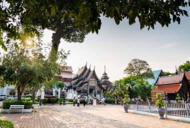 Chiang Mai, Tayland-20 Mart 2023: Öğleden sonra güneş batıyor, dışarıda, antik Lanna ahşap oymalı Budist yapısı, insanlar huzurlu avluda gezinirken.