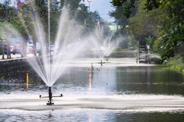 Su fıskiyeleri, Tayland 'ın kuzey başkentinin Eski Şehir Bölgesi' nin etrafını çevreleyen su kütlelerine su sıçratır. Arka planda dumanlı dağların üzerine kurulmuş trafik devam ediyor..