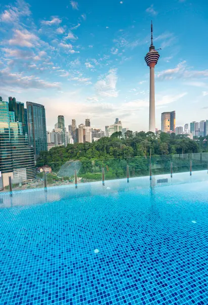 stock image Stunning rootop view of KL city and Menara Kuala Lumpur,close to sunset with blue rooftop bar infinity pool in the foreground and blue sky dotted with clouds,skyscrapers and trees in KLCC park.