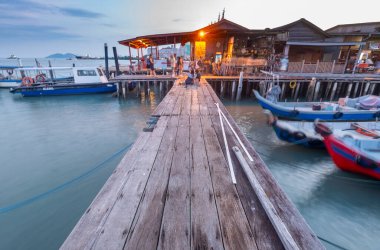Penang Adası, Malezya-25 Nisan 2023: Eski Klan Jetty kaldırımları boyunca, gün batımına yakın, ziyaretçiler durur, oturur ve kıyıda, Malacca Boğazı 'nın sularında motorlu botlarla fotoğraf çekerler..