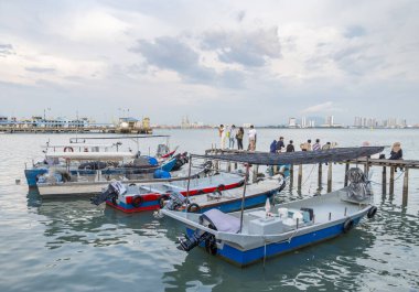 Penang Adası, Malezya-25 Nisan 2023: Eski Klan Jetty kaldırımları boyunca, gün batımına yakın, ziyaretçiler durur, oturur ve kıyıda, Malacca Boğazı 'nın sularında motorlu botlarla fotoğraf çekerler..