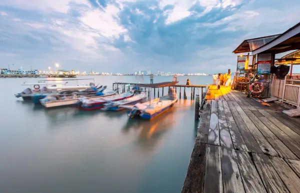 stock image Penang Island,Malaysia-April 25 2023: Along the old Clan Jetty boardwalks,near sunset,visitors stand, sit and take photos by the waterside,with motor boats in the waters of the Malacca Strait.