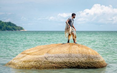 Penang, Malezya-30 Nisan 2023: Penang 'ın güney ucundaki bir sahilde, gizli bir mücevher olarak bilinen, güzel kumları, palmiyeleri, sakin ılık denizleri, mavi gökyüzü ve güneş ışığıyla yerel bir adam balık avlar..
