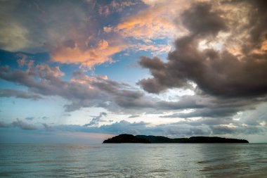 Kıyı şeridinden Andaman Denizi 'ne doğru bakan bulutlar kumlu kıyı şeridinde sürükleniyor, deniz alacakaranlıkta boşalıyor, Langkawi' nin güneybatı kıyısında önemli bir turizm merkezi..