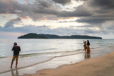 Langkawi Adası, Malezya-Mayıs 01-2023: Günbatımında, gezginler ve tatilciler gün batımına yakın, güzel, beyaz kumlarda gezinirken ve sakin denizde kürek çekerken veya yüzerken dinlenirler..