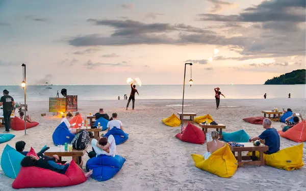 stock image Langkawi Island, Malaysia-May 01 2023:Western travelers relax on bean bags, on the fine white sand,watching flame throwers perform in front of them at dusk.