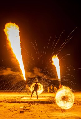 Langkawi Adası, Malezya-05 Mayıs 2023: Akşamları, günbatımından sonra, yetenekli itfaiyeciler kumsalda oturan turistlerin önünde etkileyici ateş yeme ve ateş soluma manevraları yapıyorlar..