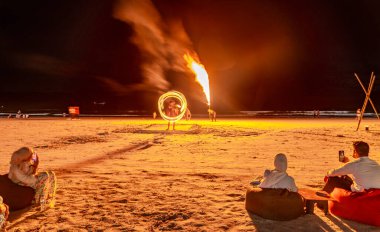 Langkawi Adası, Malezya-05 Mayıs 2023: Akşamları, günbatımından sonra, yetenekli itfaiyeciler kumsalda oturan turistlerin önünde etkileyici ateş yeme ve ateş soluma manevraları yapıyorlar..