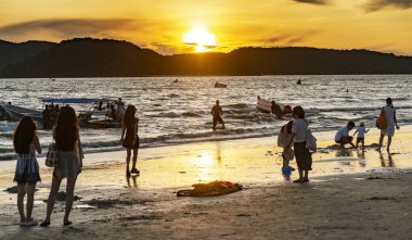 Langkawi Adası, Malezya-05 Mayıs 2023: Langkawi 'nin batı kıyısındaki küçük adaların arkasında güneş batarken, birçok insan deniz kıyısında toplanarak güzel günbatımını ve deniz kenarında oynamayı izler..