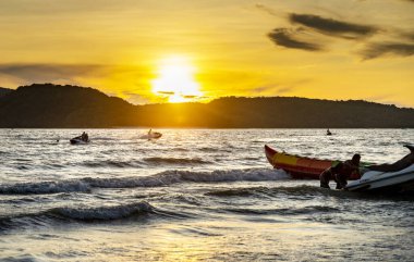 Langkawi Adası, Malezya-Mayıs 01-2023: Güneş Malezya 'nın ilerisindeki küçük adaların arkasında batıyor ve jet ski' ler dalgaların arasında kayıkları başka bir iş gününün sonunda getiriyorlar..