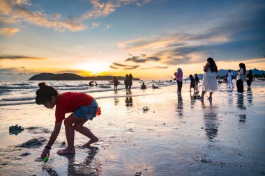 Langkawi Adası, Malezya-05 Mayıs 2023: Langkawi 'nin batı kıyısındaki küçük adaların arkasında güneş batarken, birçok insan deniz kıyısında toplanarak güzel günbatımını ve deniz kenarında oynamayı izler..