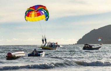 Langkawi Adası, Malezya-Mayıs 05-2023: Günbatımı yaklaşırken jet ski ve tekneleriyle deniz üzerinde parazitli bir yolculuğa çıktıktan sonra, tatilciler bir sürat teknesinin arkasına inerler..