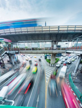 Yoğun şehir trafiğinin bulanık hareketi, kaldırımın altında hızla ilerlerken, aşağıdaki kalabalık şehrin üzerinden hızla geçen yüksek, yolcu dolu bir gökyüzü treni....