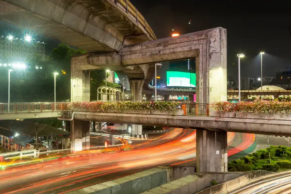 stock image Streaks of red tail lights of many vehicles rush under huge concrete columns, massive civil condtruction,supporting Bangkok's extensive urban rail network.