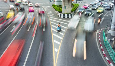 Bangkok, Tayland-08 Mayıs 2023: Bir motosikletli taksi şoförü sabırla oturur, hareketsiz, onu çevreleyen yoğun trafik hatlarına karışmayı bekler, arabalar, otobüsler ve bisikletler hızla geçerken.