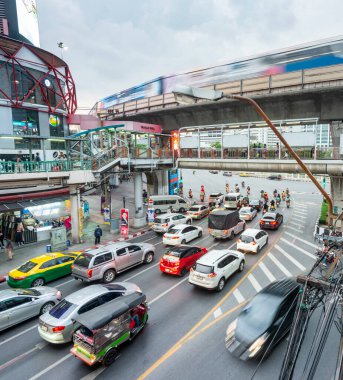 Bangkok, Tayland-08 Mayıs 2023: Şehir ulaşımı, trafik ışıklarında bekleyen çok sayıda araç ve yolcu dolu banliyö treni yüksek demiryolu boyunca hızla ilerliyor.