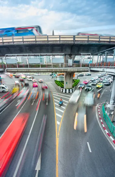 stock image Bangkok,Thailand-May 08 2023:A motorcycle taxi rider sits patiently,motionless,waiting to blend in with the endless lines of busy traffic surrounding him,as passenger filled trains cross above.