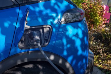 Worcester,England,UK-September 17 2024:Parked domestic electric,battery powered car,with charging connector attached ,being charged during the day,at a public railway station car park.