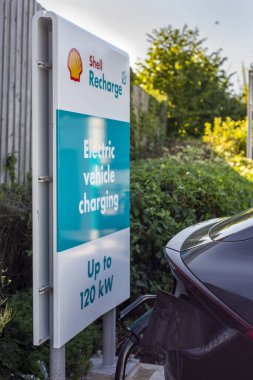 Worcester, İngiltere, İngiltere-17 Eylül 2024: Park halindeki yerli elektrik, pil motorlu araba, şarj cihazı takılı, gün boyunca şarj ediliyor, büyük bir süpermarket otoparkında.