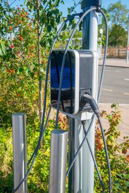 EV şarj noktası, bir tren istasyonunun otoparkında, kamu elektrikli aracının park yerinin yanında duruyor..