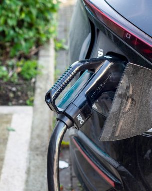 Park halindeki elektrikli araba, şarj konnektörü takılı, kamu elektrikli aracının şarj edildiği bir yerde, kamu tren istasyonunun otoparkında..