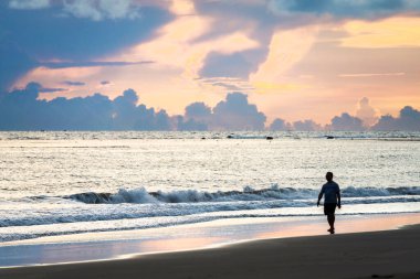 Luzon Adası, Filipinler - 22 Mayıs 2023: Bir insan figürü deniz kıyısında, sakin kumlarda, kuzeybatı Filipinler 'de, günbatımında geziniyor..