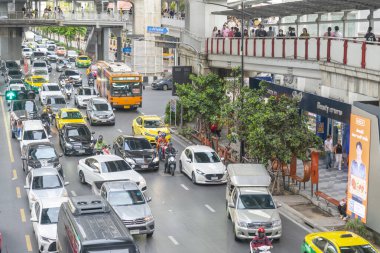Bangkok, Tayland-Temmuz 03: 2024: Birçoğu banliyö yollarında yürüyen, yaya köprülerini, Skytrain istasyonlarını ve dükkanları birbirine bağlayan, çok sayıda sıkışık araç aşağıda yavaşça hareket ediyor.
