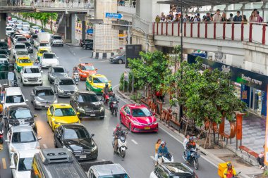 Bangkok, Tayland-Temmuz 03: 2024: Birçoğu banliyö yollarında yürüyen, yaya köprülerini, Skytrain istasyonlarını ve dükkanları birbirine bağlayan, çok sayıda sıkışık araç aşağıda yavaşça hareket ediyor.
