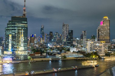 Bangkok, Tayland-02 Temmuz: Nehir yaşamının gece sahnesi, aydınlatılmış şehir silueti ve nehir tekneleri, en üst kattan, çok amaçlı ikonik bir binanın açık terası, nehir kenarı binası.