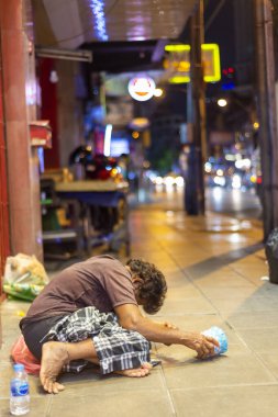 Bangkok, Tayland-Temmuz 04: 2024: Sokaklarda yaşayan yarı bilinçli bir birey, elinde bir kupayla kaldırıma çömelmiş, insanların biraz bozukluk vermesini bekliyor.