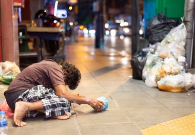 Bangkok, Tayland-Temmuz 04: 2024: Sokaklarda yaşayan yarı bilinçli bir birey, elinde bir kupayla kaldırıma çömelmiş, insanların biraz bozukluk vermesini bekliyor.