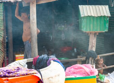 Kamboçya-21 Şubat 2024: Phnom Krom tapınağının altındaki köyde, bir Khmer ailesi, Siem Reap şehrinin birkaç mil güneyinde, iyi şans getirmesi için basit konutlara ve küçük yeşil Buda evine bakıyor..