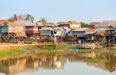 Öğleden sonra geç saatlerde, küçük bir gölün yanında, Phnom Kraom Tepesi tapınağının altında duran basit konutlar, yağmur mevsiminde bölgeyi sel basar..