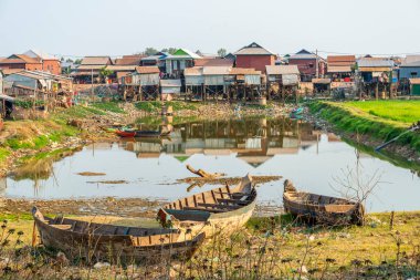 Öğleden sonra güneş ışığı altında, su birikintisinin yanında, Phnom Kraom Tepesi tapınağının altında duran basit konutlar, yağmur mevsiminde bölgeyi sel basar..
