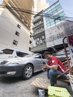 Tayland-Nisan 07 2024-Araba park görevlileri 88 katlı yapının altında, mavi gökyüzüne ve yukarıdaki güneş ışığına bakan gölgede oturuyorlar..