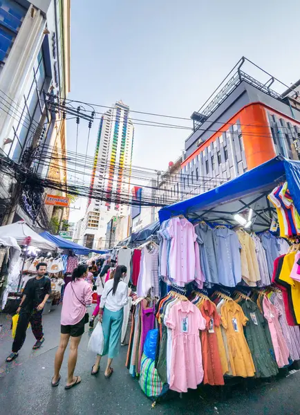 Tayland-Nisan 07 2024 İnsanlar sokak seviyesinde giysi raflarına göz gezdirirken, ikonik bir apartman binası gibi, şehir simgesi uzaklarda beliriyor..