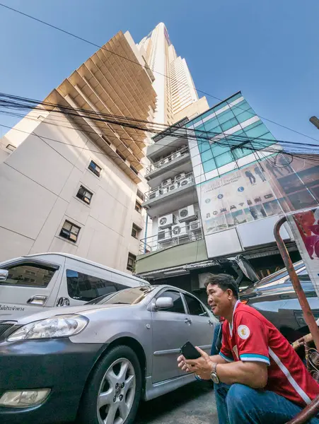 Tayland-Nisan 07 2024-Araba park görevlileri 88 katlı yapının altında, mavi gökyüzüne ve yukarıdaki güneş ışığına bakan gölgede oturuyorlar..