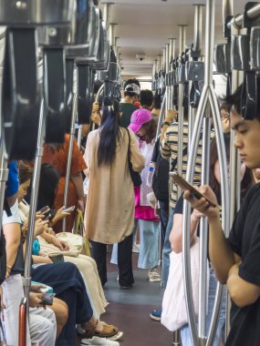 Bangkok, Tayland-30 Haziran 2024: Bir BTS Skytrain vagonunda, şehir merkezine doğru bir yolculukta, öğleden sonra, yolcular nispeten daha rahat bir şekilde seyahat ederler..