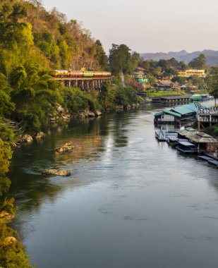 A passenger diesel locomotive train,carrying tourists,moving slowly and carefully across a section of the wooden trestle bridge,next to a sheer cliff face and a steep long drop on the other side.