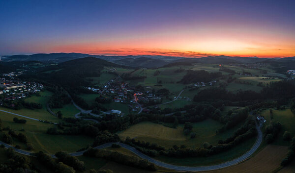 Aerial view with a drone of the village of Grueb near the town of Grafenau in the Bavarian Forest at summer solstice at blue hour sunset in twilight, Germany