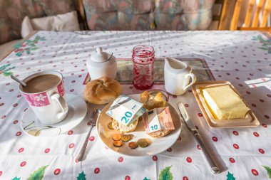 Kahvaltı masasını kahve şekerli süt ve tereyağlı kahvaltı masası ve avro paraları ve banknotlarla kaplı rulo banknotlar, Almanya