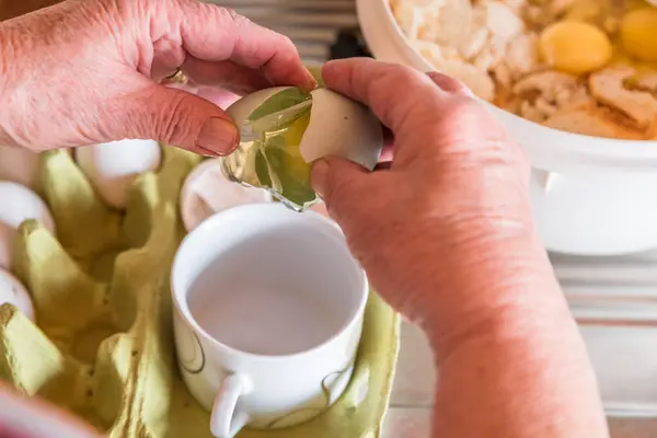 stock image Good bourgeois housewife woman cook in kitchen beating eggs and separating yolk from white with cup to make bread dumplings with bread crumbs, Germany