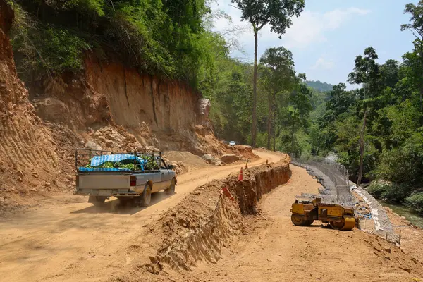 A pickup truck transports a truck full of fresh bananas. road construction is going on. A country road route through a valley along a river where the road is damaged during the rainy season.