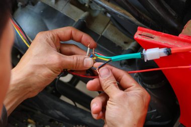 Motosikletin elektrik sistemini onarmak için kabloları bağlayan araba tamircisinin elindeki renkli kabloların yakın plan görüntüsü..