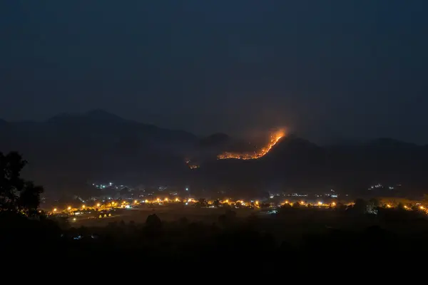 night landscape On a night, a forest fire spread on the mountain. The village is surrounded by mountains, with city lights and forest fires standing out. in Chiang Mai, Thailand
