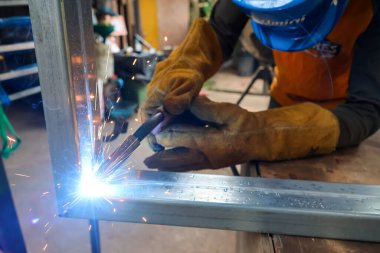 Kaynak makinesiyle kaynak yapıldıktan sonra galvanize metal bir kıvılcım yarattı. Koruyucu deri eldivenler giyen kaynakçı.