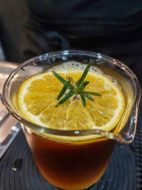 Limon suyuyla karıştırılmış kahve bardağında dilimlenmiş limon. Üstünde biberiye yaprakları var. Dükkanda limonla karıştırılmış kahve ferahlatıcıdır.